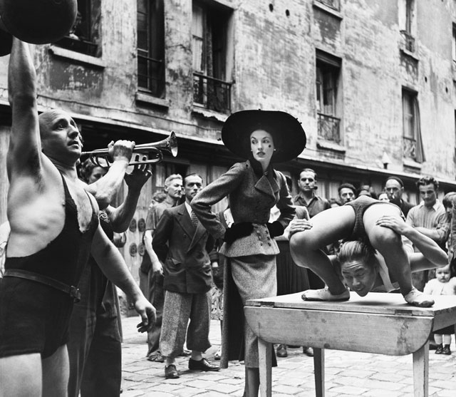 Elise Daniels with street performers, suit by Balenciaga, Le Marais, Paris, 1948. Photograph by Richard Avedon © The Richard Avedon Foundation.