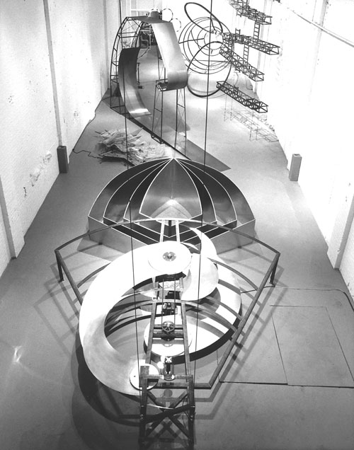 Alice Aycock. The Thousand and One Nights in the Mansion Of Bliss, Part II, The Fortress Of Utopia (Fata Morgana), 1983
The Glance of Eternity: steel, galvanized sheet metal, Plexiglas, motorized parts; 3 ½ h x 14 w x 15 l ft. The Cookie Cutter: galvanized sheet metal; 4’ high x 12’ wide x 10’ long. The Loop to Loop: four elements- steel; 12’ high x 2 ½’ wide x 60’ long Camera Obscura: steel, brass, Styrofoam, plaster. Double Somersault: steel and blinking lights. Wave-Making Machines: two elements- painted wood, steel, motorised parts. The Tree of Life: galvanised sheet metal; 10’ high x 14’ wide. General von Hutier’s Infiltration Tactics: red-orange neon lights, steel; 50’ long. Croissant Cutter: steel, 3’ diameter x 10’ long. Photograph: Luigi Kurmann.