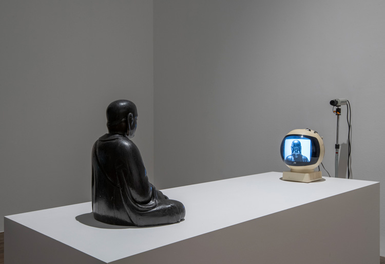 Nam June Paik. TV Buddha 1974. Installation view, Tate Modern 2019. 18th century wooden sculpture, closed-circuit television camera and JVC Videosphere cathode-ray tube television. Stedelijk Museum, Amsterdam. Photo: © Tate (Andrew Dunkley).