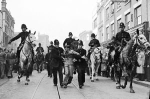 Eddie Worth. An anti-fascist demonstrator is taken away under arrest after a mounted baton charge during the Battle of Cable Street, London, 4 October 1936. © Alamy.